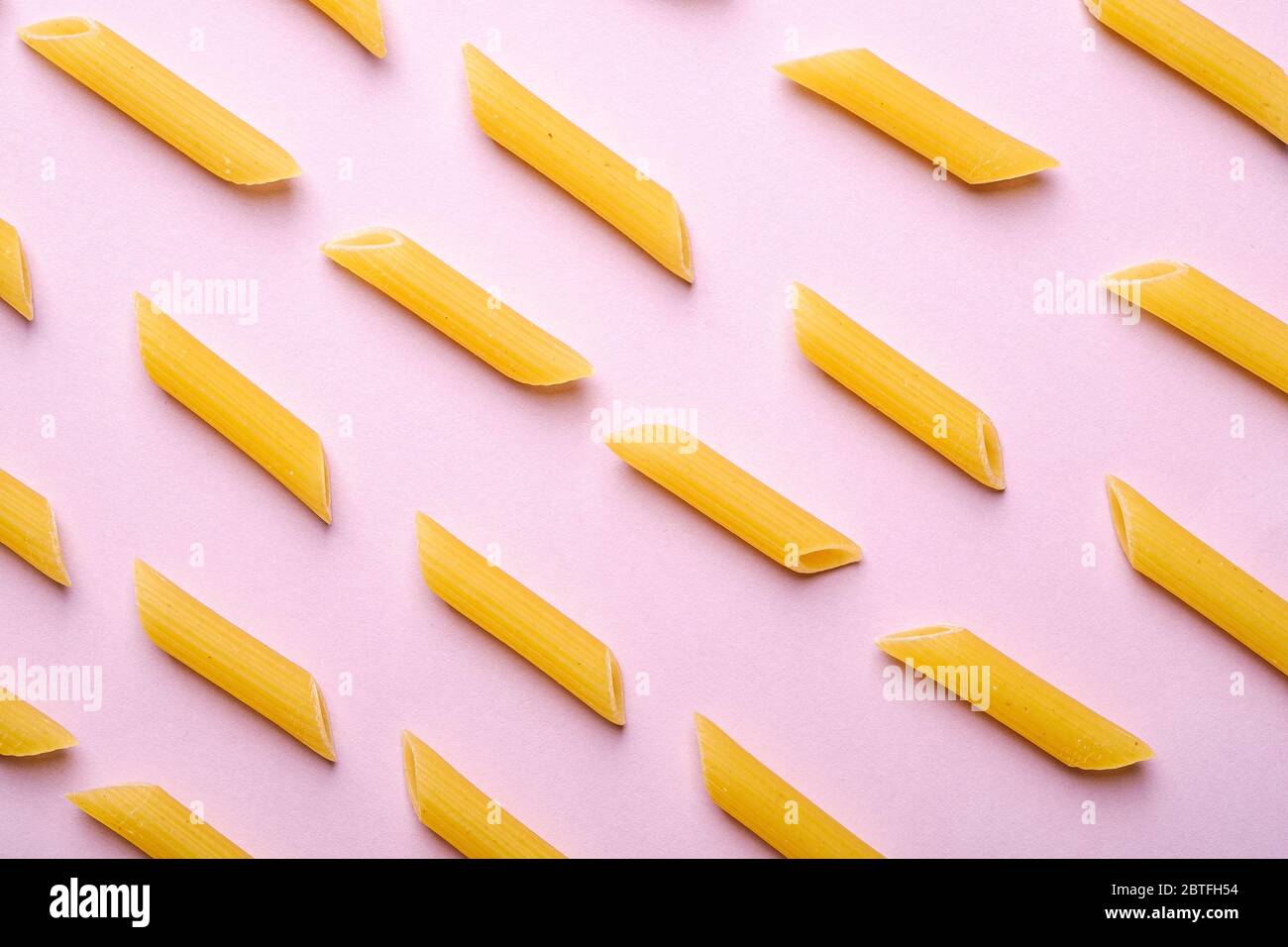 Pâtes italiennes, tube de penne cru macaroni motif sur fond rose, vue de dessus, nourriture abstraite Banque D'Images