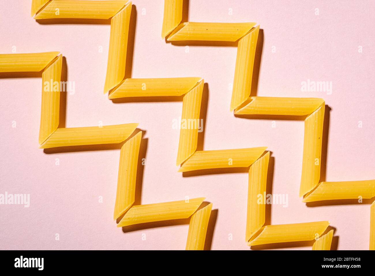 Pâtes italiennes, tube de penne cru macaroni en zigzag sur fond rose, vue du dessus, nourriture abstraite Banque D'Images