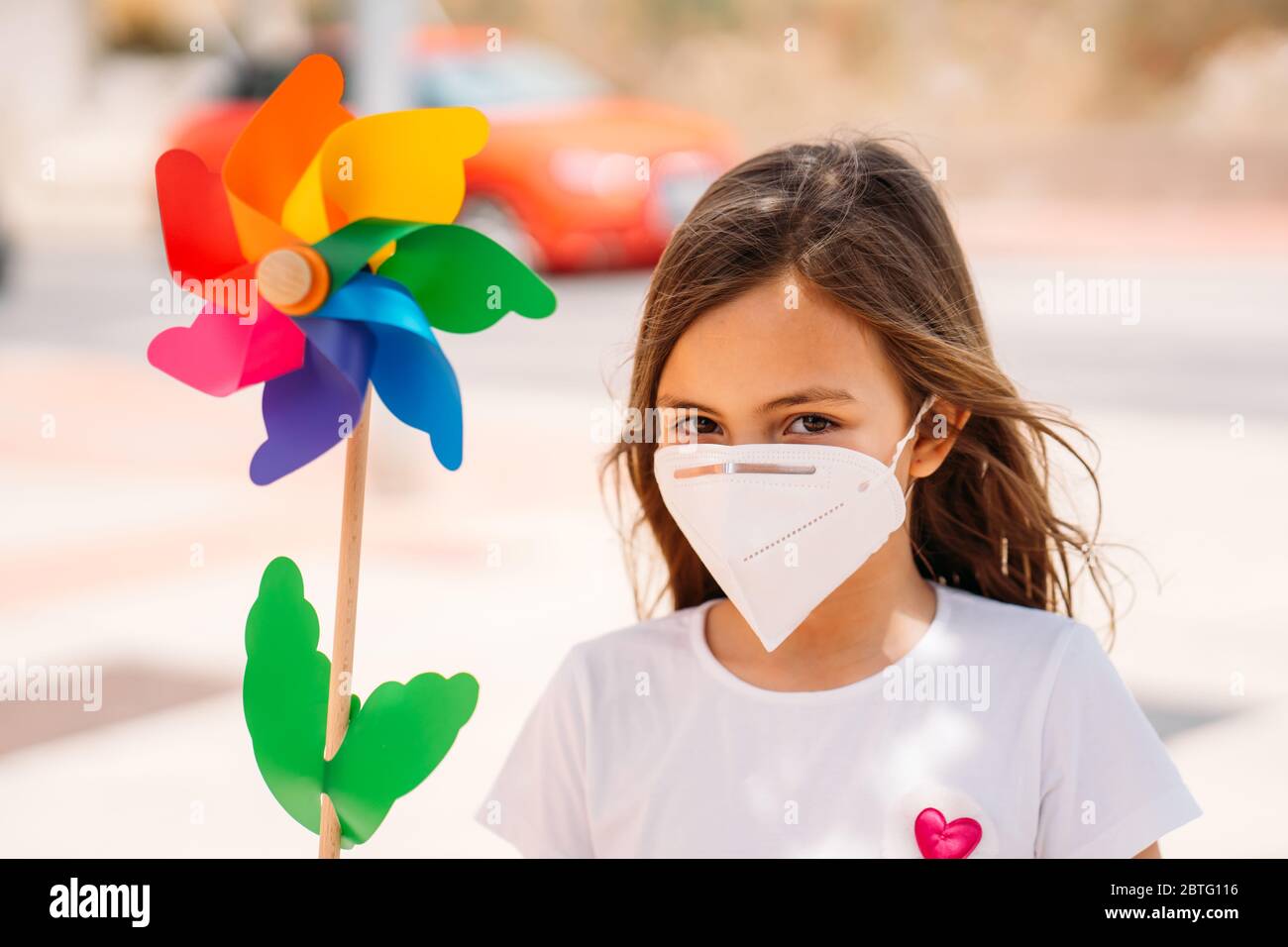 Petite fille portant un masque et tenant un jouet coloré moulin à vent, ou roue de pin. Banque D'Images