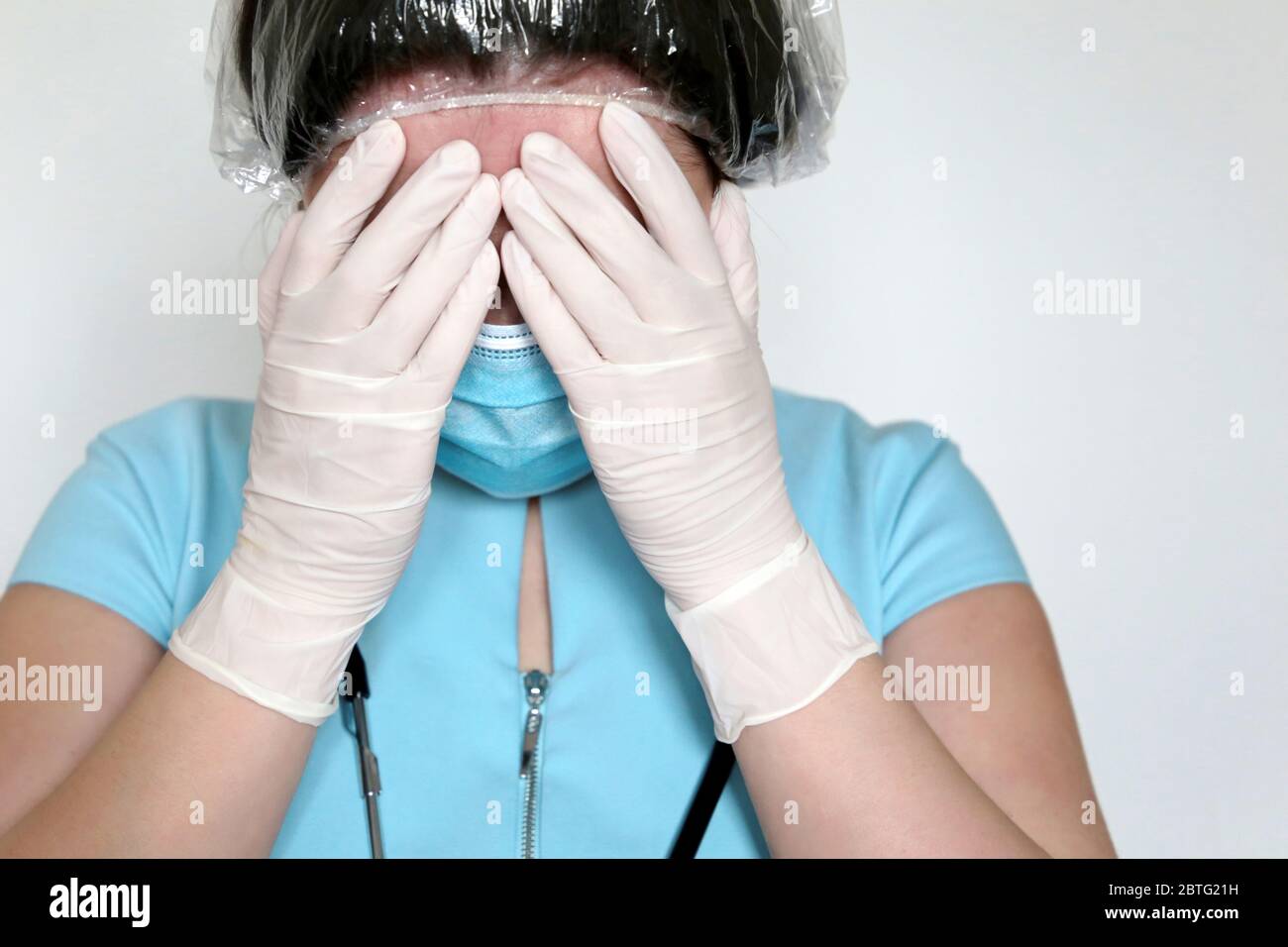 Femme en masque médical et gants en latex couvre son visage avec les mains. Un médecin contrarié ou fatigué après un travail acharné, concept de traitement du coronavirus Covid-19 Banque D'Images
