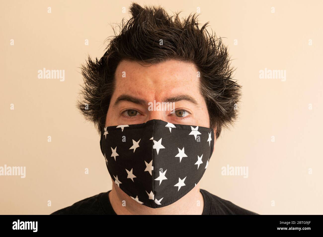 Un homme de la fin de la trentaine avec un masque réutilisable regardant directement le spectateur pendant la pandémie du coronavirus Covid 19 avec des cheveux de verrouillage fous Banque D'Images
