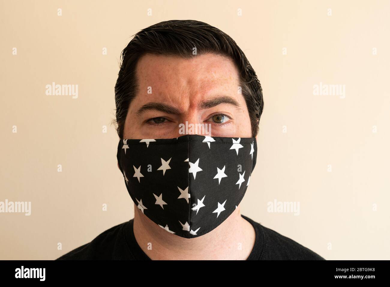 Un homme de la fin de la trentaine avec un masque réutilisable sur son nez et sa bouche, regardant directement le spectateur pendant la pandémie du coronavirus Covid 19 Banque D'Images