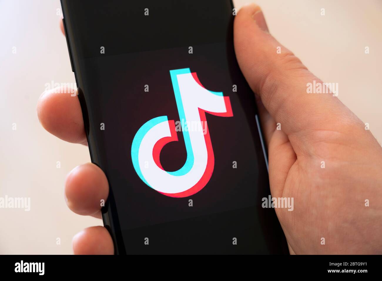 Main d'un homme tenant un smartphone affichant un grand logo pour l'application chinoise de partage de vidéos sur les réseaux sociaux Tik Tok Banque D'Images