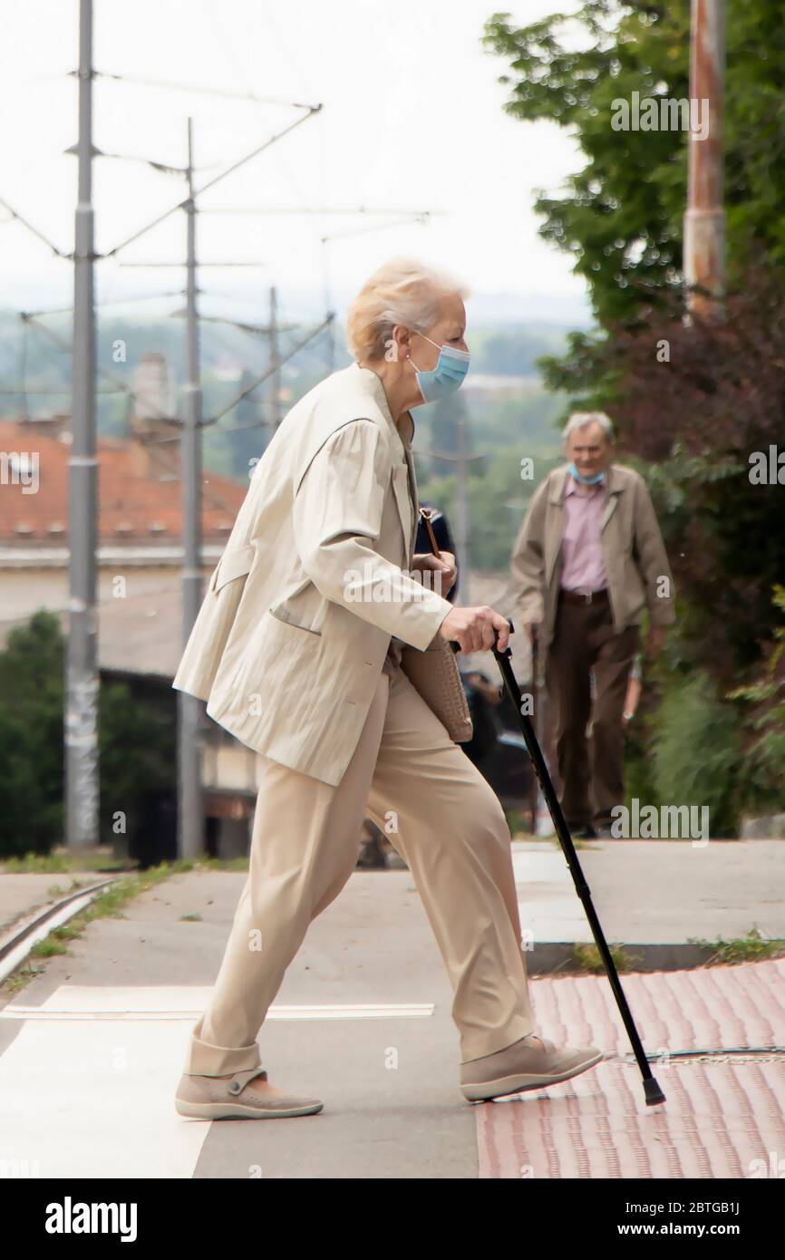 Belgrade, Serbie - 21 mai 2020: Femme âgée portant un masque chirurgical de visage marchant avec une canne sur le passage de zébrures Banque D'Images