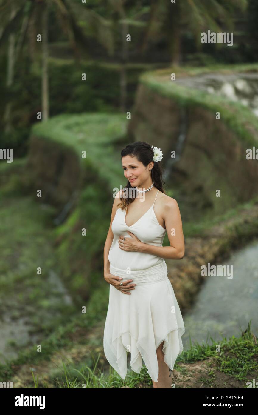 Jeune femme enceinte en robe blanche avec vue sur les rizières en terrasses de Bali dans la lumière du soleil du matin. Harmonie avec la nature. Concept de la grossesse. Banque D'Images