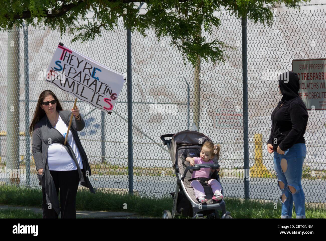 Baltimore, Maryland, États-Unis. 25 mai 2020. Une femme debout près d'une  petite fille dans une poussette/un landau et une autre femme dans un sweat  à capuche, tient le signe lisant « ils