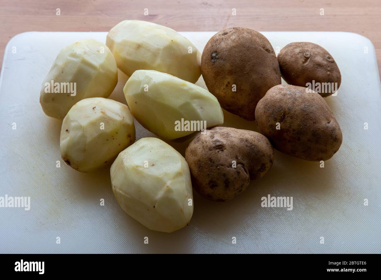 Les pommes de terre blanches non cuites sont sur une planche à découper, la moitié d'entre elles étant pelées. Banque D'Images