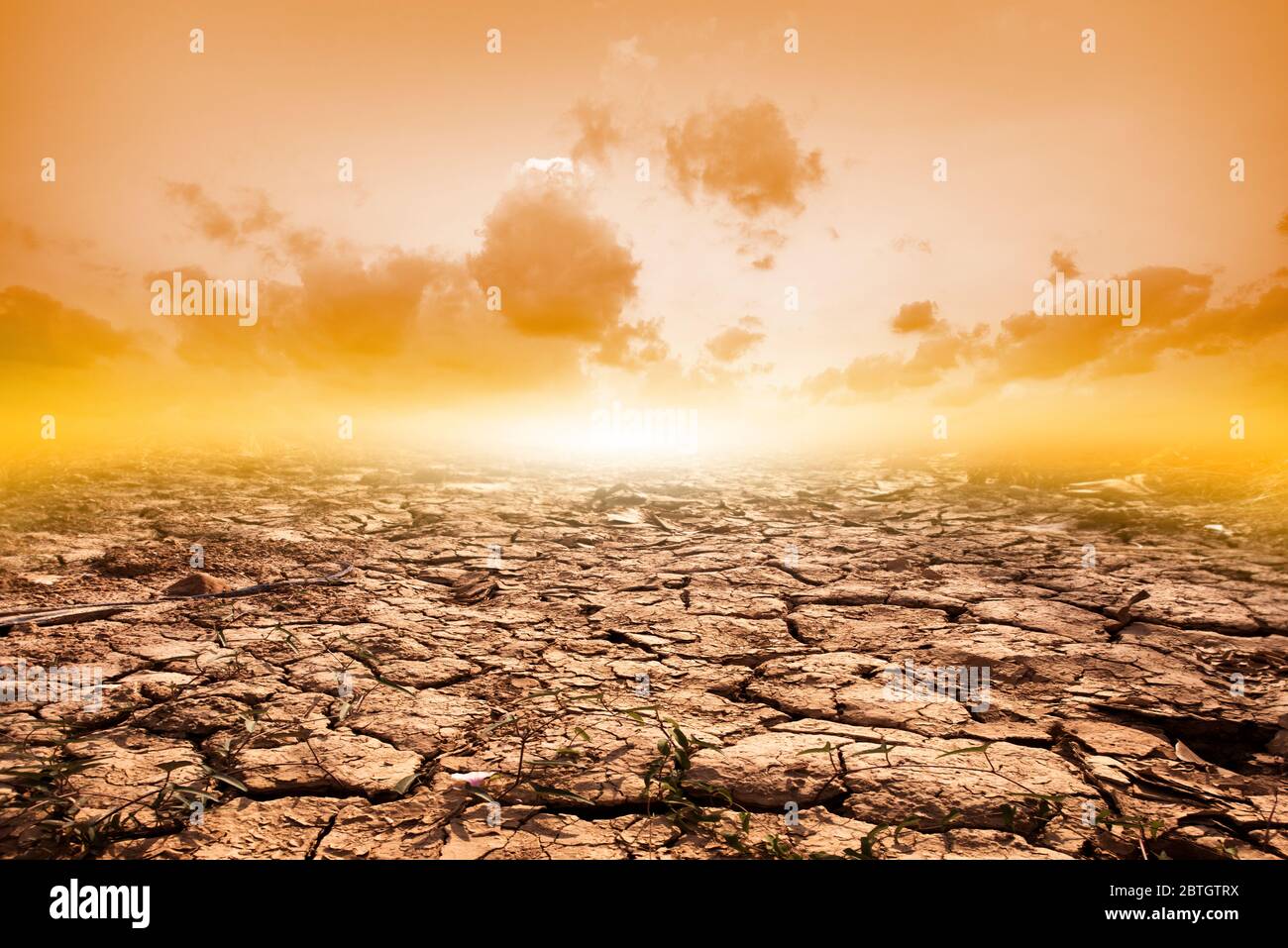 Sol fissuré en été avec le coucher du soleil ou des fissures du sol séché en saison aride sur fond de ciel orange. Réchauffement climatique Banque D'Images