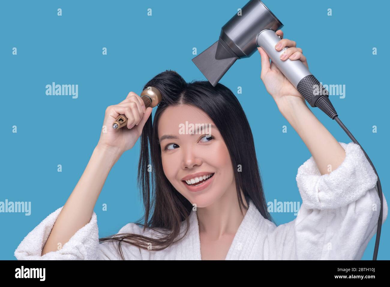 Brunette jeune femme asiatique sèche ses cheveux et souriant Banque D'Images