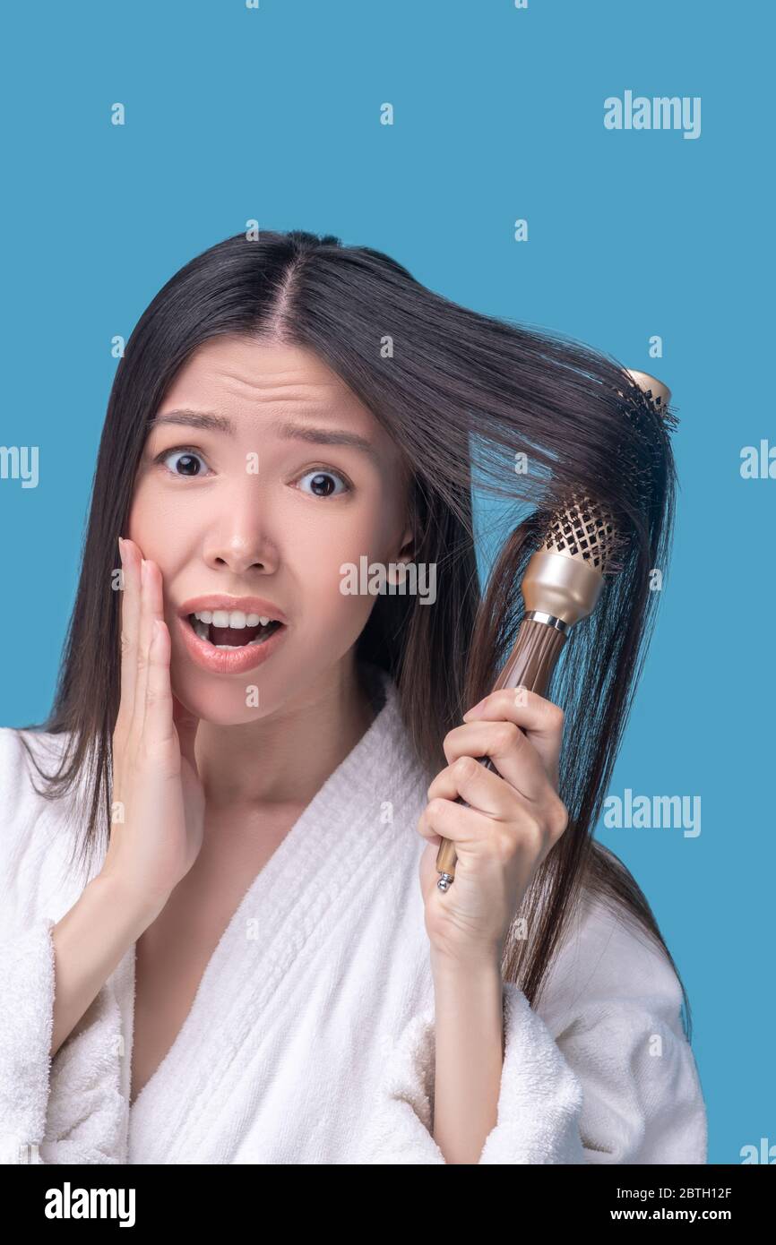 Femme asiatique aux cheveux foncés se brossant les cheveux et se sentant stressée Banque D'Images