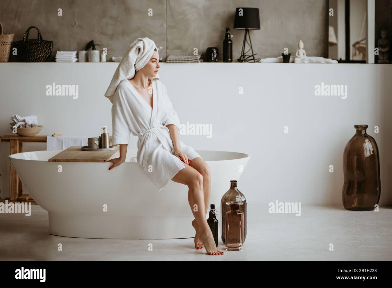 Belle jeune femme en peignoir assis sur le bord de la baignoire. Banque D'Images
