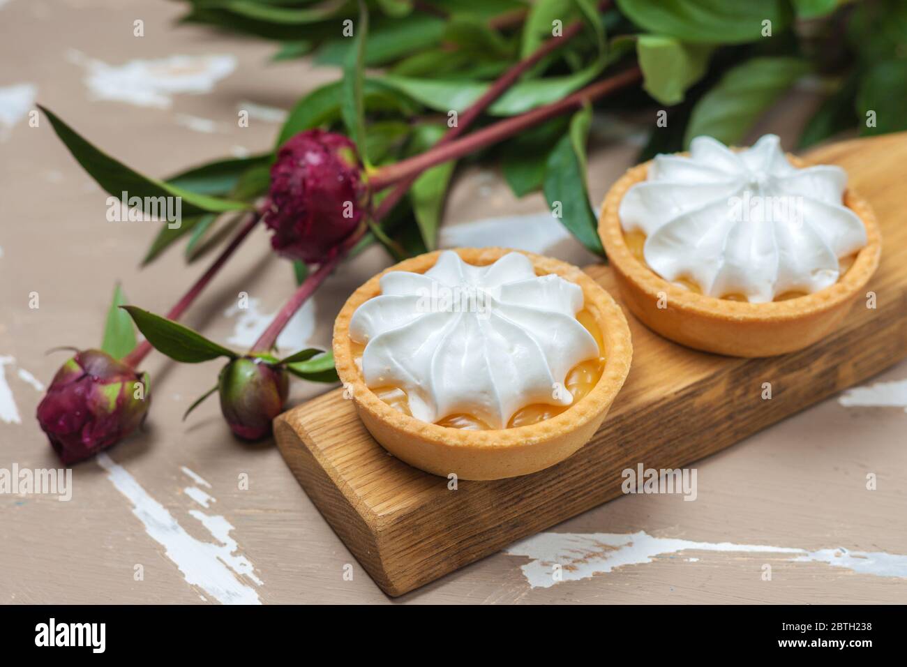 Tarte au citron. Deux gâteaux sur une assiette en bois et trois fleurs de pivoine Banque D'Images