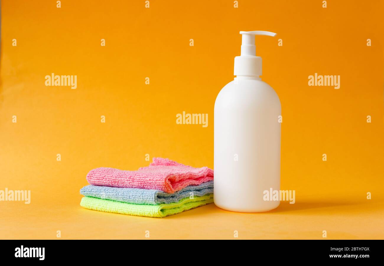 Trois serviettes de nettoyage colorées et une bouteille blanche pour nettoyer les sols sur fond jaune. Banque D'Images