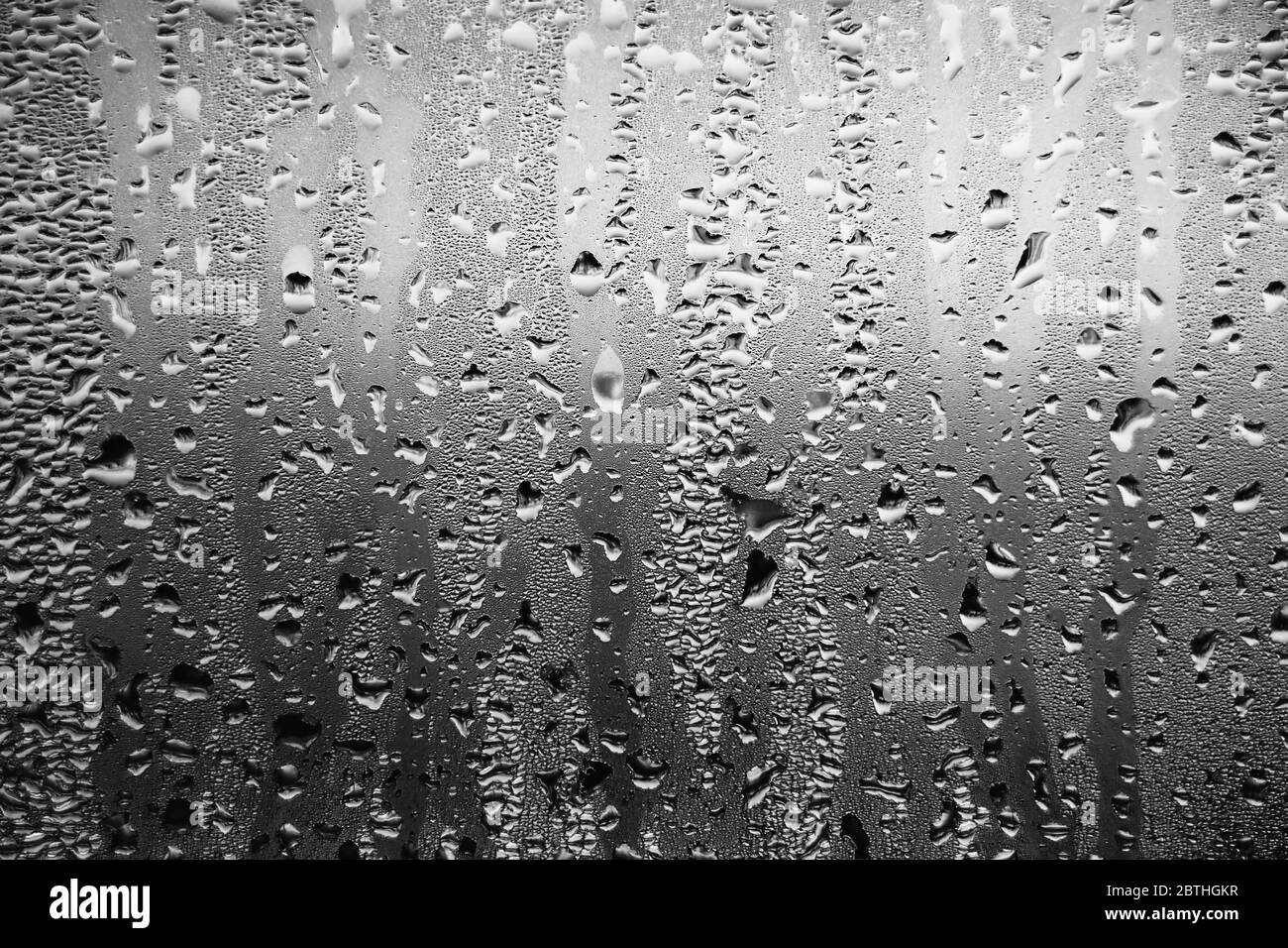 Arrière-plan noir et blanc représentant des gouttes de pluie qui s'enrament sur la vitre par temps sombre et sombre et nuageux. Mélancolie. Banque D'Images