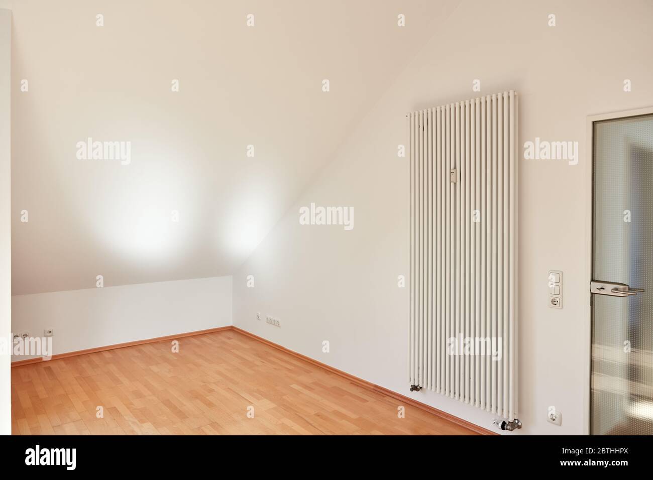 Chambre lumineuse vide avec plafond en pente dans appartement mansardé avec radiateur Banque D'Images