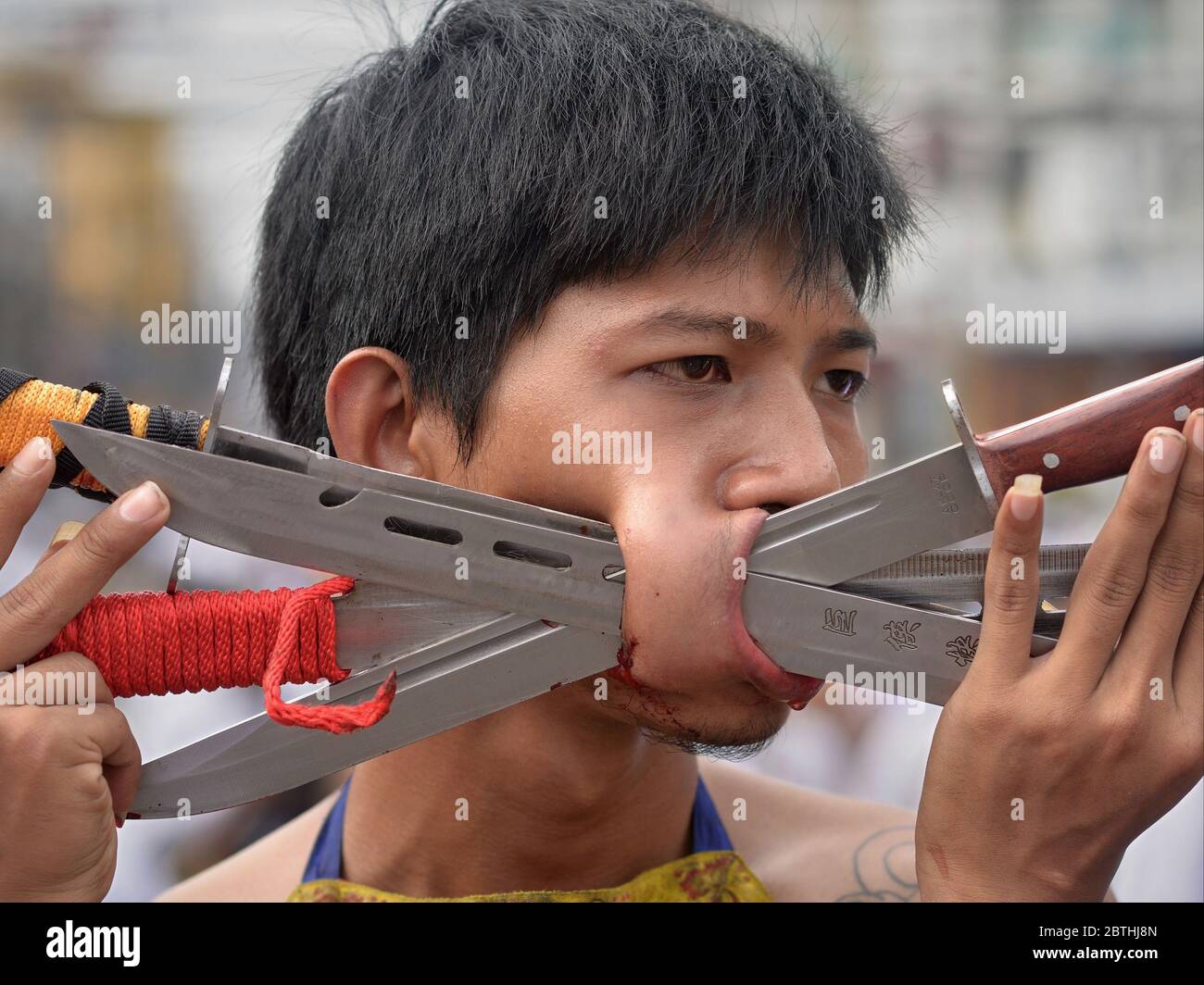 Le dévot taoïste chinois thaïlandais pière sa joue droite avec de longs couteaux pendant le Festival végétarien de Phuket. Banque D'Images