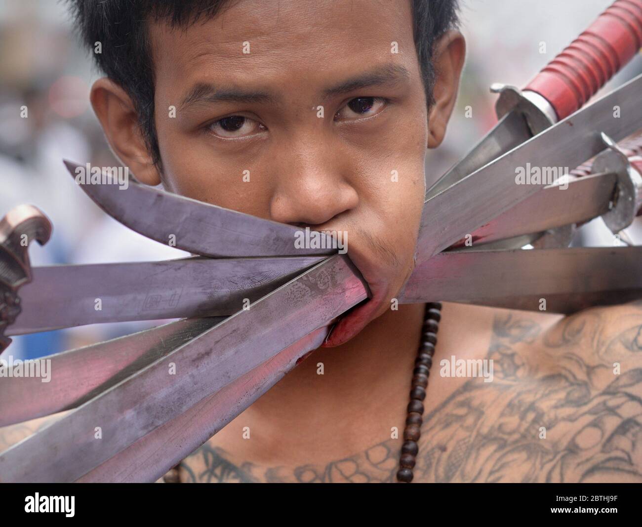 Le dévot taoïste chinois thaïlandais pière sa joue gauche avec de longs couteaux pendant le Festival végétarien de Phuket. Banque D'Images