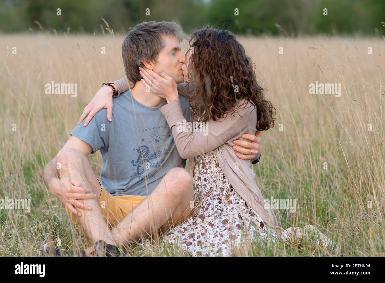 Un jeune beau couple séduisant sourire ensemble dans un beau champ extérieur montrant leur amour pour les uns les autres et embrassant Banque D'Images