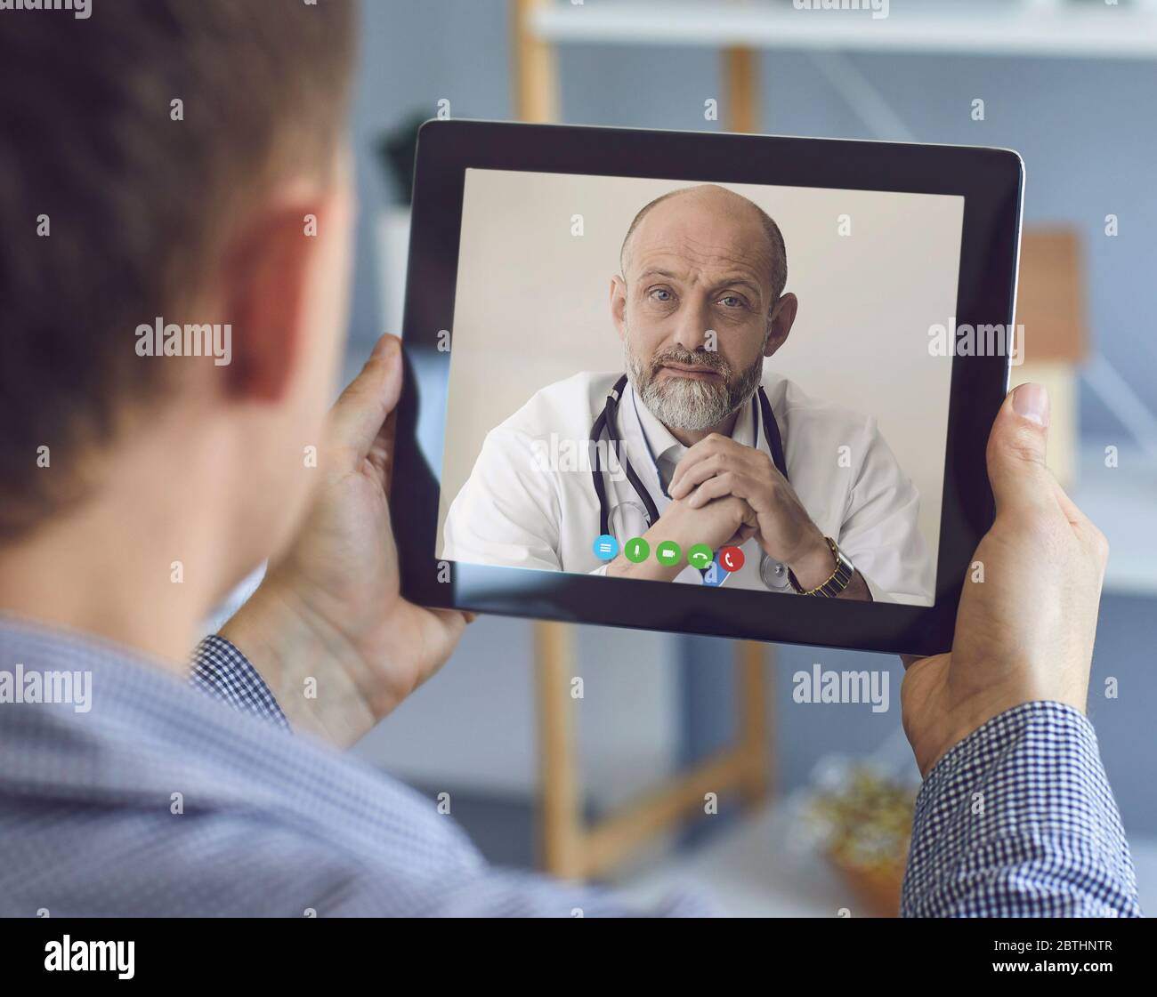 Médecin et patient en ligne. Un patient avec une tablette passe un appel vidéo à une conférence téléphonique avec un médecin pratiquant en ligne à domicile. Banque D'Images