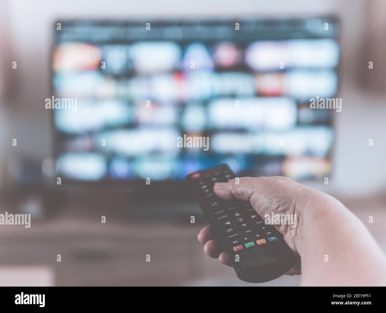 Gros plan d'une main tenant une télécommande de téléviseur tout en regardant des émissions sur un service de diffusion de télévision - filtre désaturé avec un arrière-plan flou Banque D'Images
