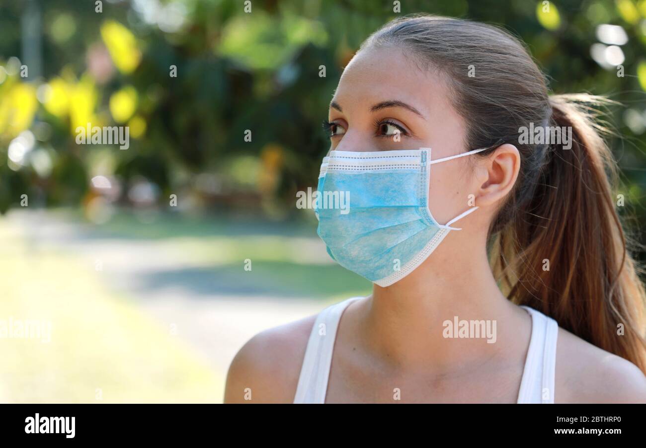 Une jeune fille de forme physique en gros plan portant un masque chirurgical dans le parc en regardant sur le côté. Portrait d'une jeune femme sportive avec masque de protection contre coron Banque D'Images