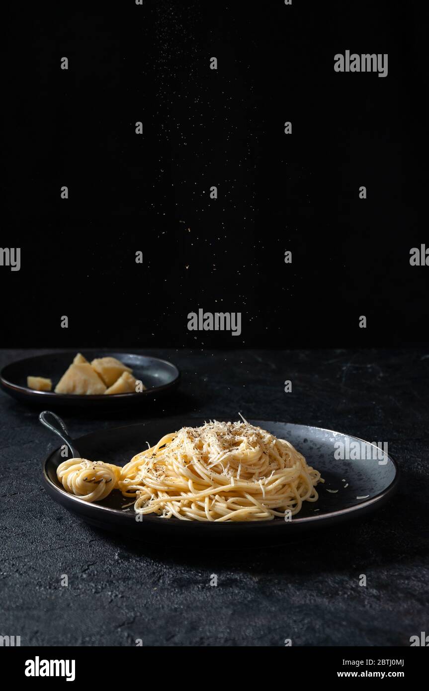 Cacio e Pepe - pâtes italiennes au fromage et au poivre sur une assiette noire sur fond sombre. Banque D'Images