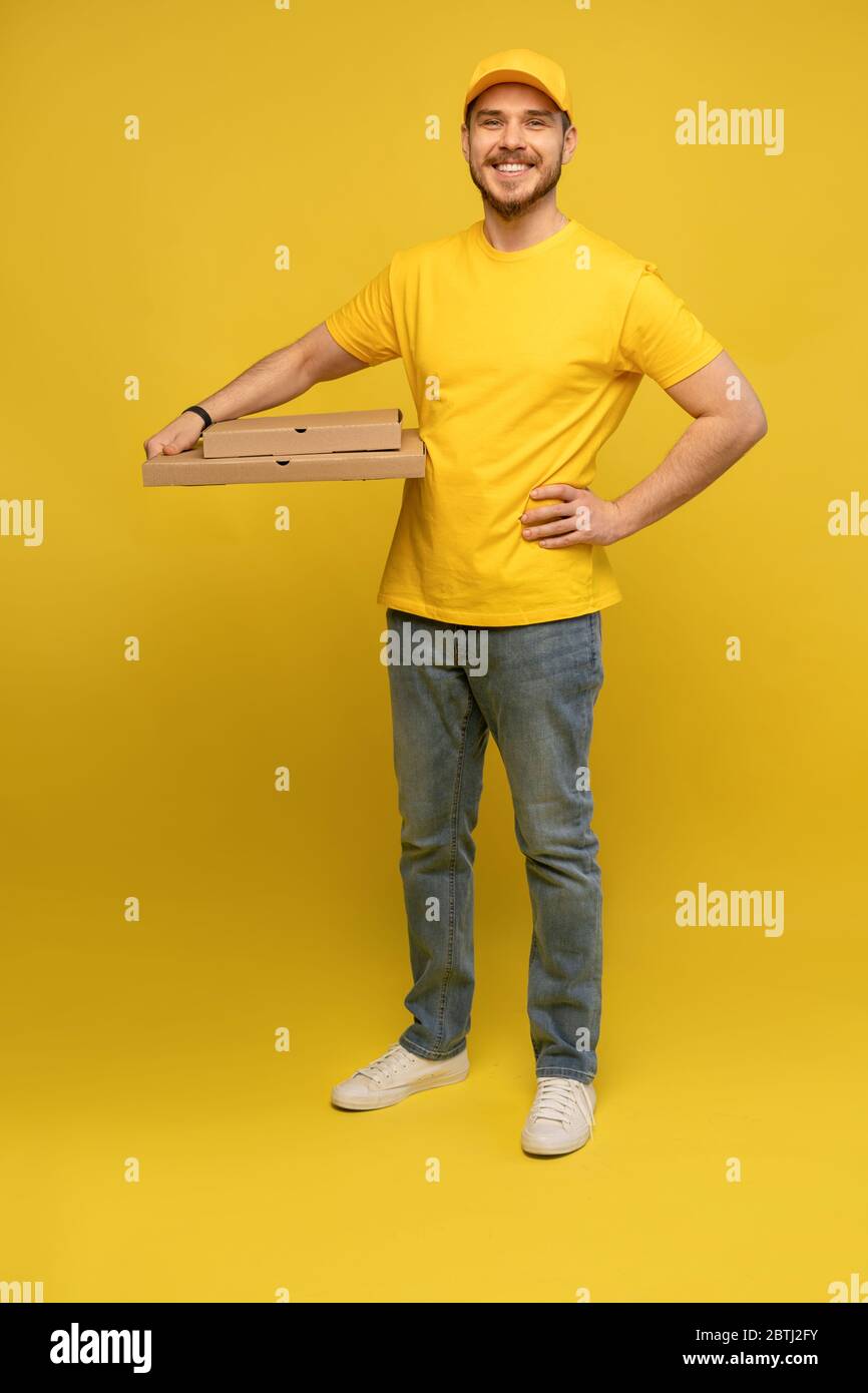 Portrait du jeune livreur en uniforme jaune avec des boîtes à pizza isolées sur fond jaune. Banque D'Images
