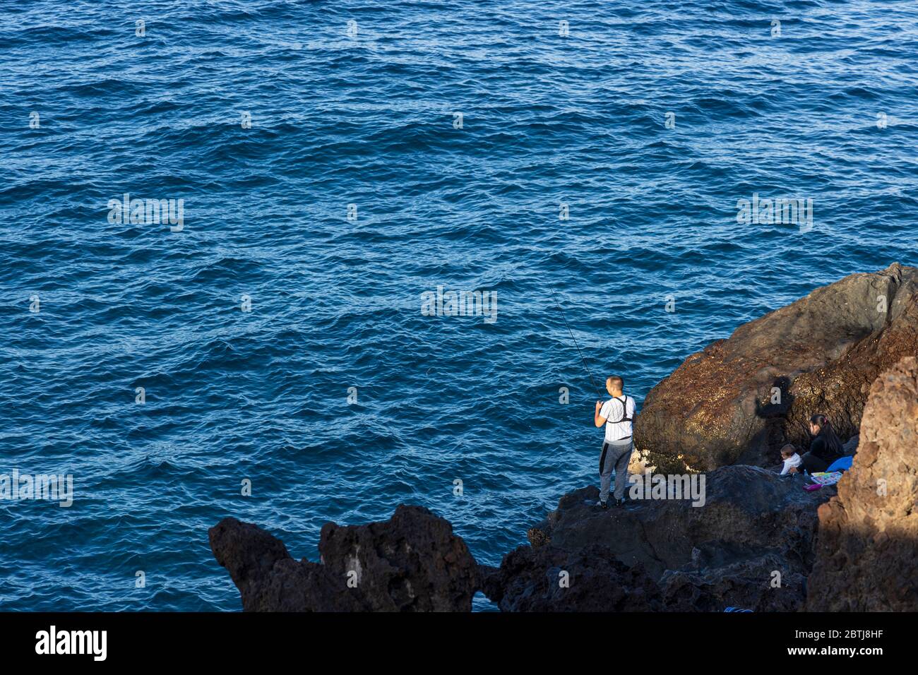 Homme pêchant sur les rochers avec femme et enfant assis derrière, tôt le matin, pendant la phase deux de la désescalade de l'état d'urgence, Covid 1 Banque D'Images