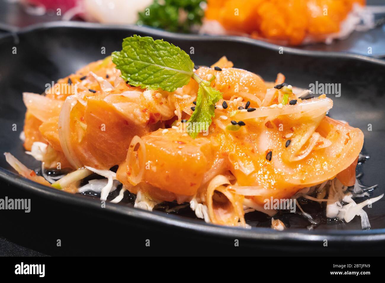 Salade de dés de saumon épicée de style thaïlandais nommée légume et herbe de yum. Servi sur une assiette noire en céramique blanche. Banque D'Images