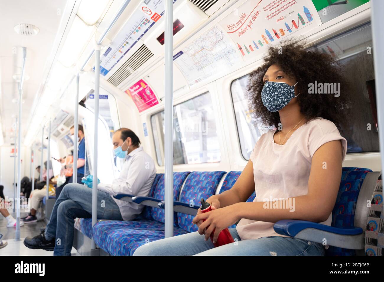 Les personnes qui voyagent pour la ville portent des revêtements faciaux et transportent des bouteilles d'eau dans le métro de Londres lorsqu'elles retournent au travail. Mai 2020 Banque D'Images