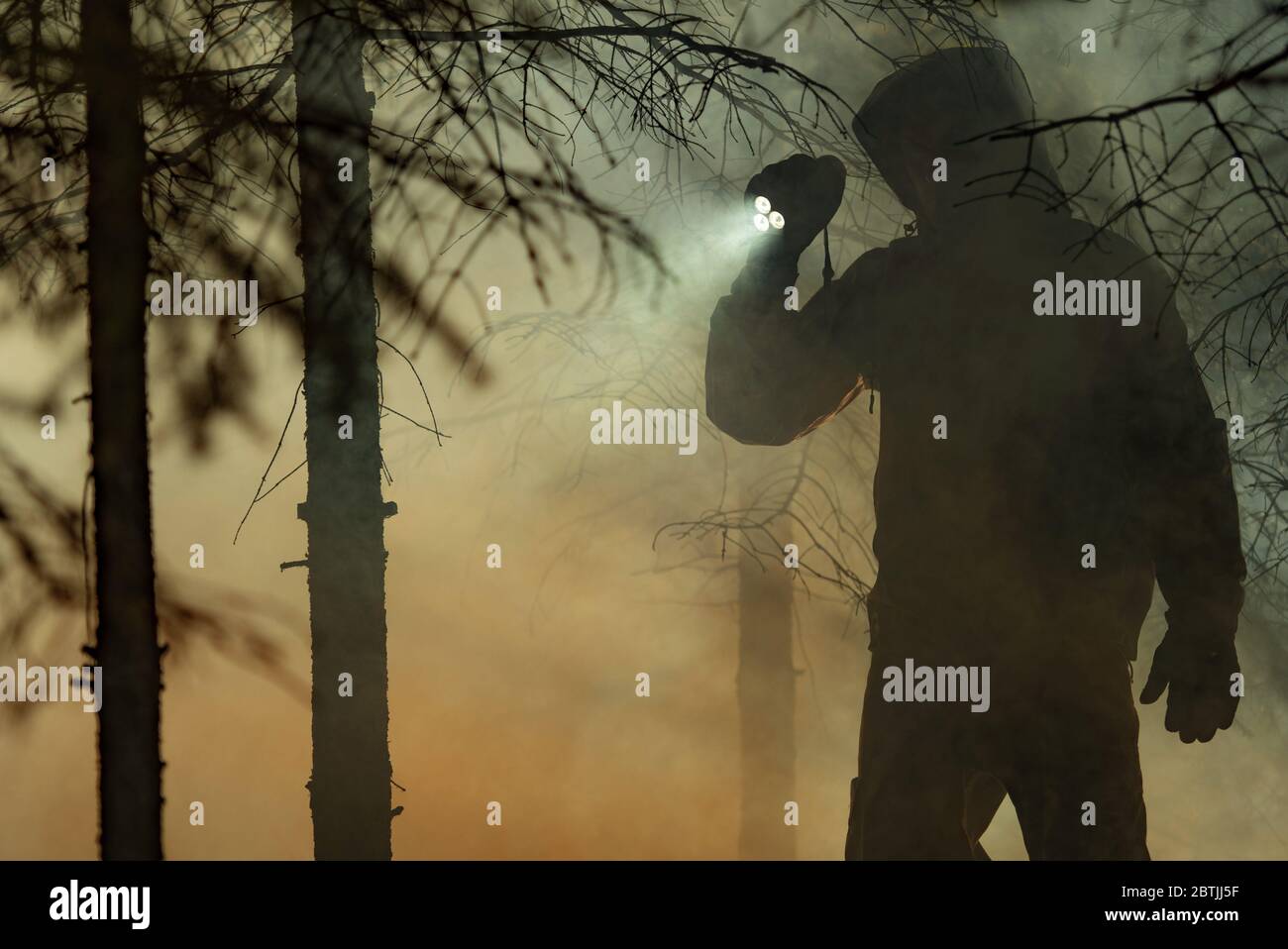 Recherche de secours. Hommes portant des vêtements de camouflage avec une puissante lampe de poche entre les arbres et la fumée de feu. Mission de sauvetage des incendies de forêt. Banque D'Images