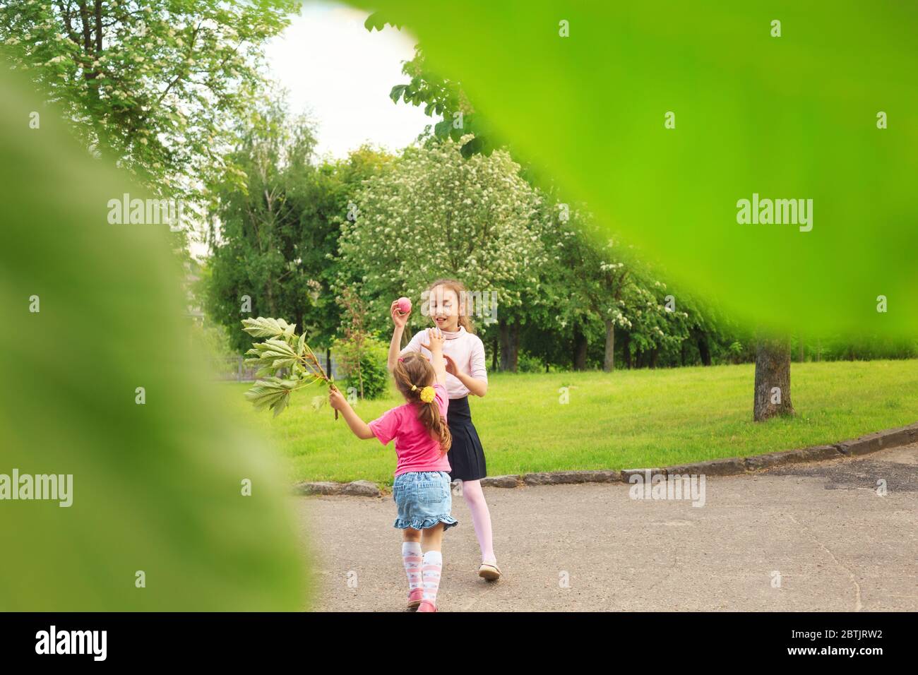 Deux petites sœurs adorables sautant avec un jouet coloré en montgolfière à l'extérieur. Les enfants souriants s'amusent dans le jardin de printemps vert les jours d'été. Banque D'Images