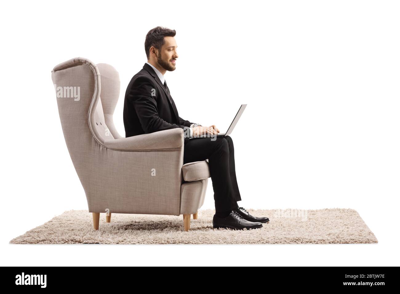 Homme dans un costume assis dans un fauteuil travaillant de la maison sur un ordinateur portable isolatedon fond blanc Banque D'Images Homme dans un costume assis dans un fauteuil travaillant de la maison sur un ordinateur portable isolatedon fond blanc Banque D'Images