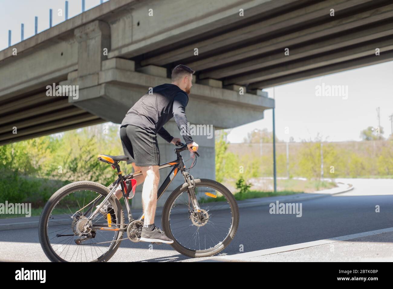Cycliste sur une route à ciel ouvert jusqu'à l'athlète du coucher du soleil, un cycliste barbu, se déplace sur l'autoroute à bord d'un vélo sportif. Sous le pont. Extérieur. S Banque D'Images