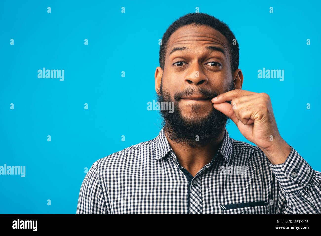Je ne dirai PAS UN mot. Homme barbu noir faisant des lèvres de zipping geste avec la main, montrant qu'il tiendra un secret, bleu studio Banque D'Images