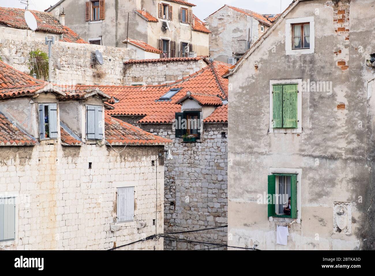 Une femme croate légèrement cachée dans la fenêtre de sa maison pendant qu'elle regarde son téléphone mobile, la vieille ville, Split, Croatie Banque D'Images