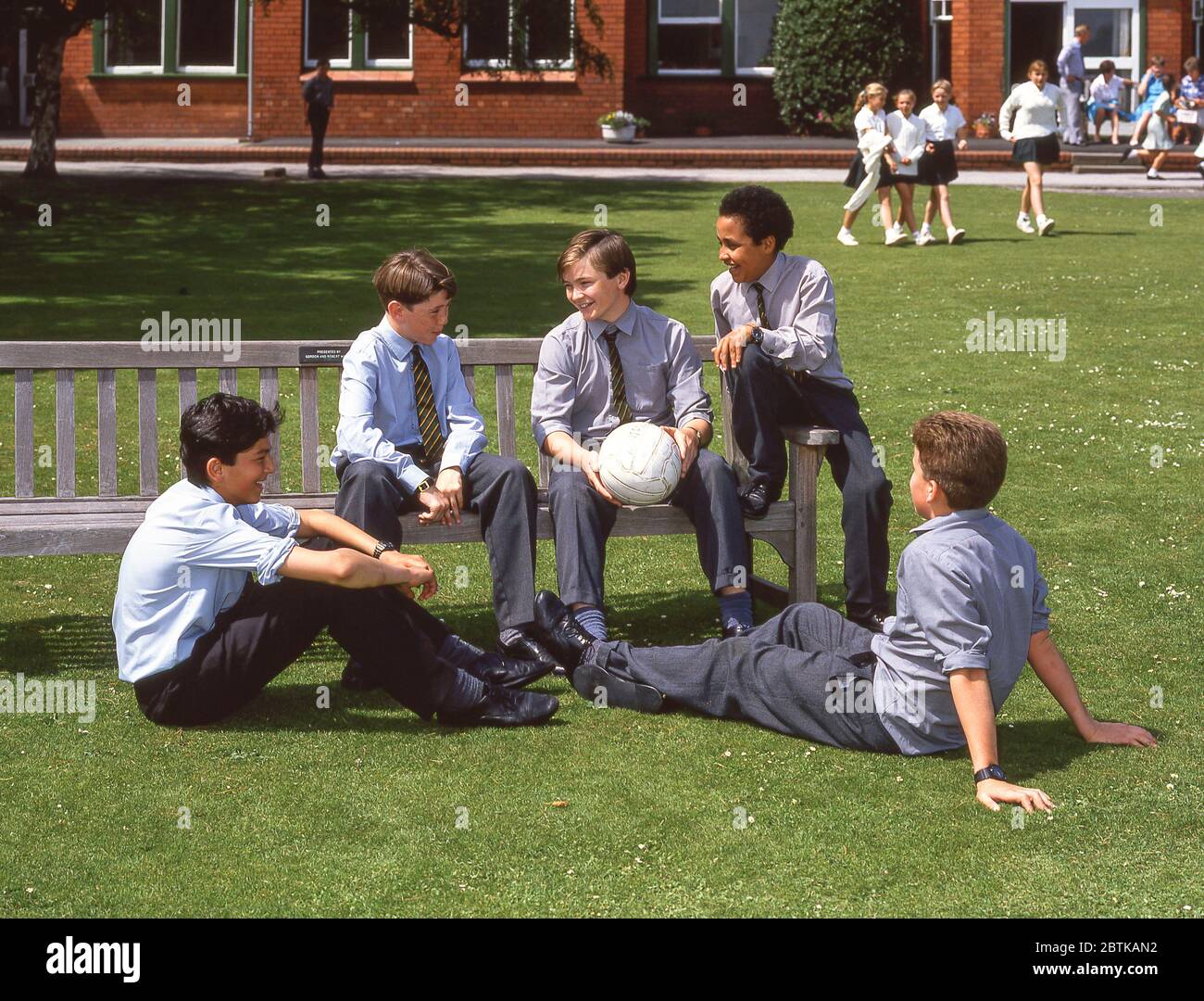 Garçons d'école assis dans le terrain d'école tenant le football, Surrey, Angleterre, Royaume-Uni Banque D'Images