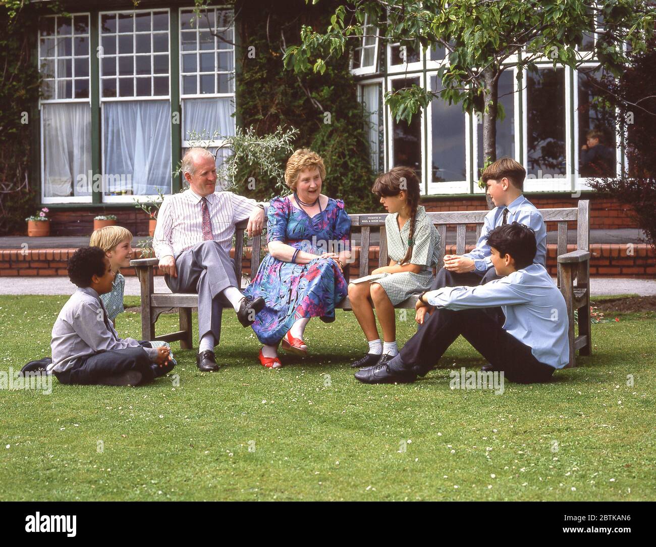Enfants et enseignants assis et parlant dans les terrains scolaires, Surrey, Angleterre, Royaume-Uni Banque D'Images