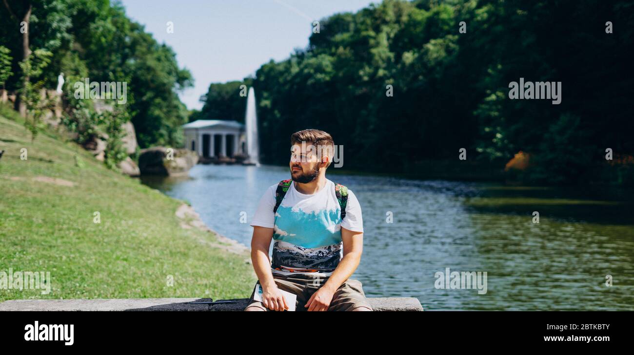 Parc Sofia, Uman. Beau homme avec un sac à dos assis sur un banc de pierre dans le parc. Jeune homme sur le fond du lac avec une grande fontaine. A m Banque D'Images
