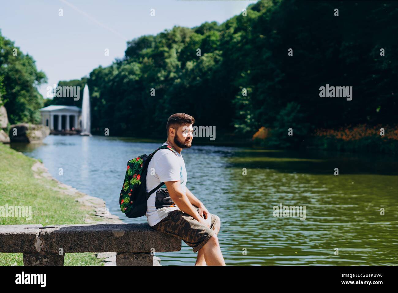 Parc Sofia, Uman. Beau homme avec un sac à dos assis sur un banc de pierre dans le parc. Jeune homme sur le fond du lac avec une grande fontaine. A m Banque D'Images