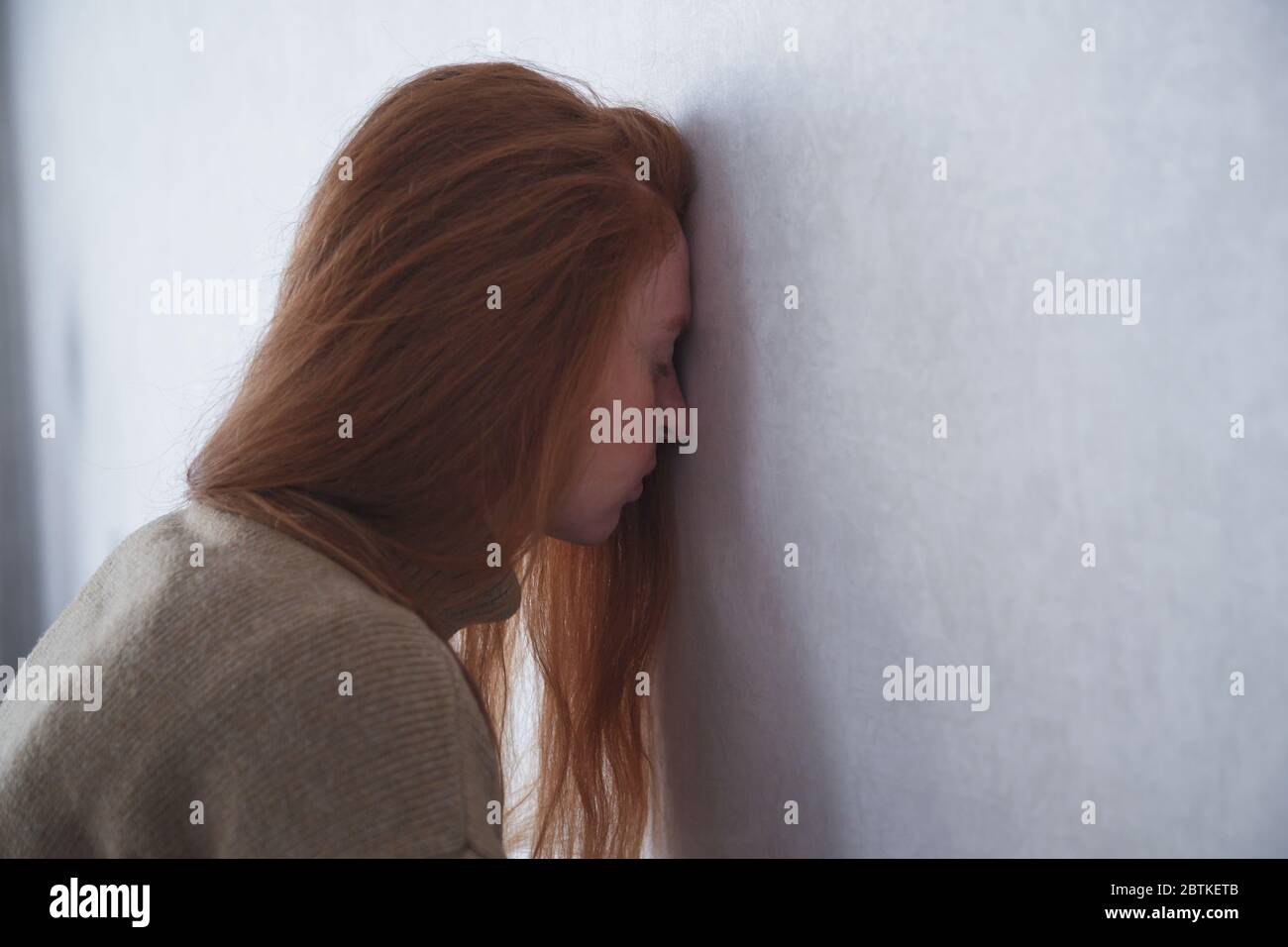 Une jeune femme à tête rouge désespéré et déprimée penche son front sur le mur à la maison. Banque D'Images