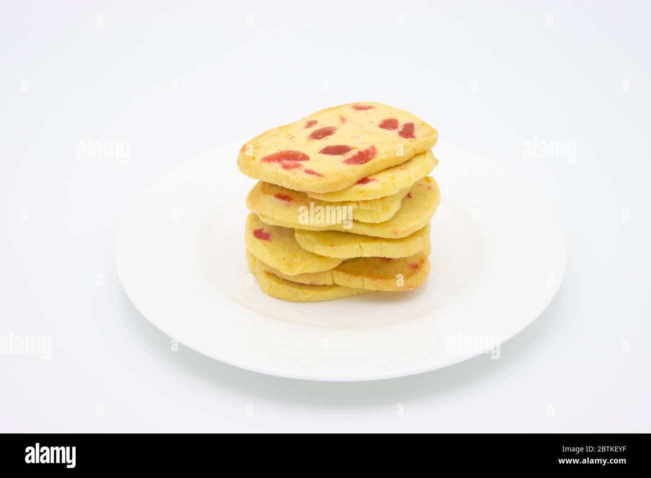 Un tas de biscuits traditionnels croustillants, de biscuits dorés faits maison avec des morceaux de cerise rouge présentés sur une assiette blanche Banque D'Images