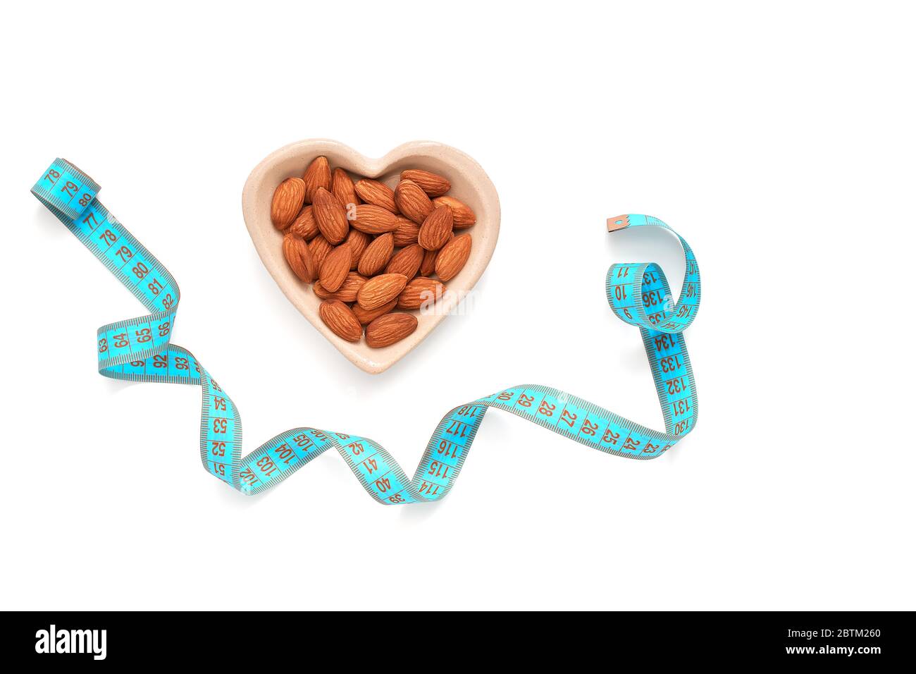 Amandes dans un bol en forme de coeur et ruban de mesure bleu isolé sur fond blanc. Le concept de perte de poids et de nourriture de régime. Vue de dessus, plan d'appartement Banque D'Images