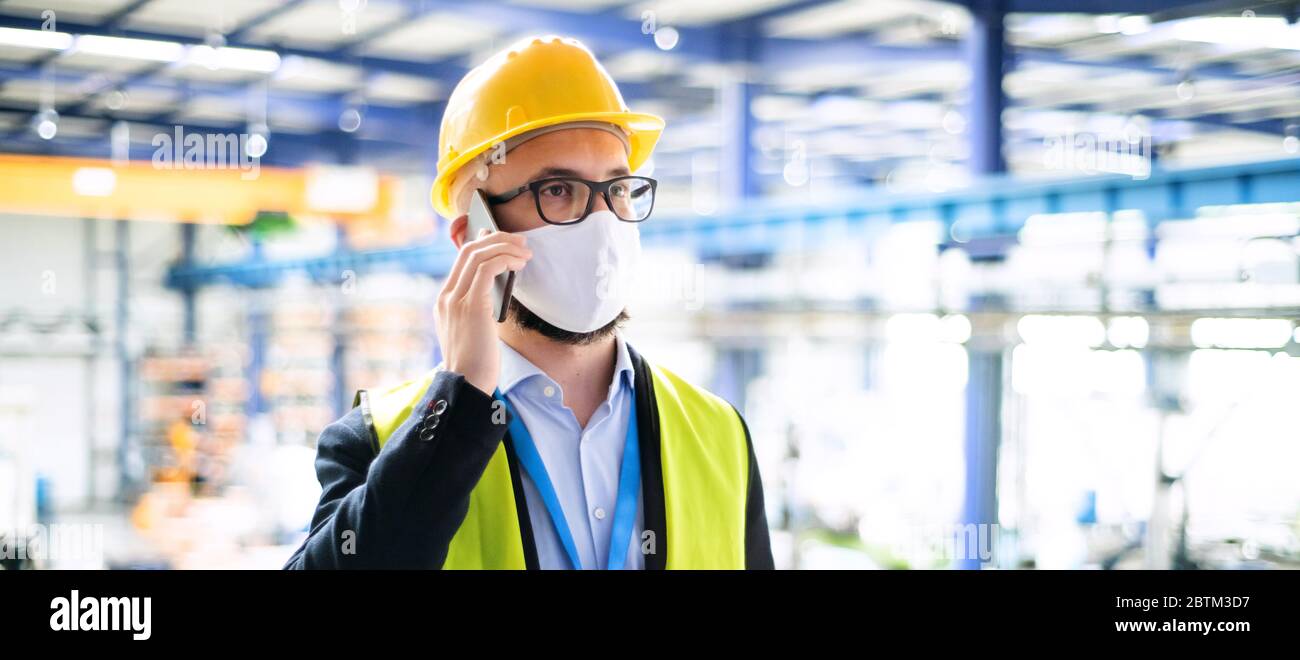 Technicien ou ingénieur avec masque de protection et casque travaillant en usine. Banque D'Images