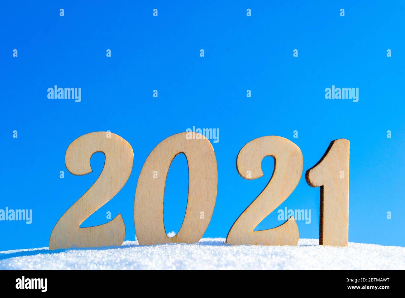 Célébration du nouvel an 2021. Figures en bois 2021 sur une surface naturelle enneigée d'hiver. Illuminée par le soleil brillant contre un ciel bleu clair. Style naturel Banque D'Images