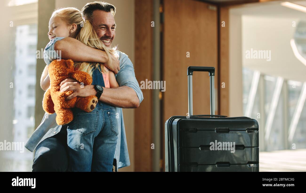 Heureux père arrivant à la maison et saluant sa fille avec un câlin. voyageur embrassant son enfant alors qu'il entre dans la porte h. Banque D'Images