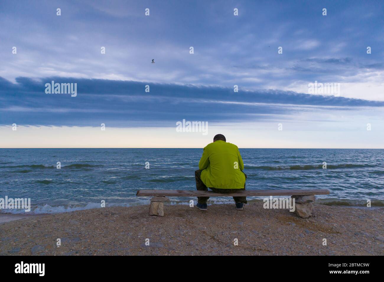 Homme assis sur un banc près d'une plage et regardant sur l'océan avec des nuages épiques. Banque D'Images