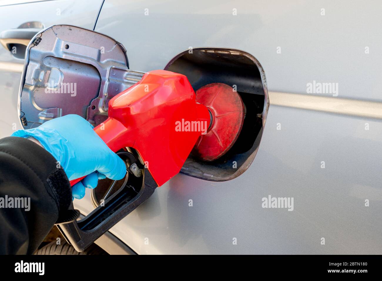 Main portant un gant de protection individuel bleu pompe le gaz dans une automobile. Faible profondeur de champ, concentration sur la pompe. Banque D'Images