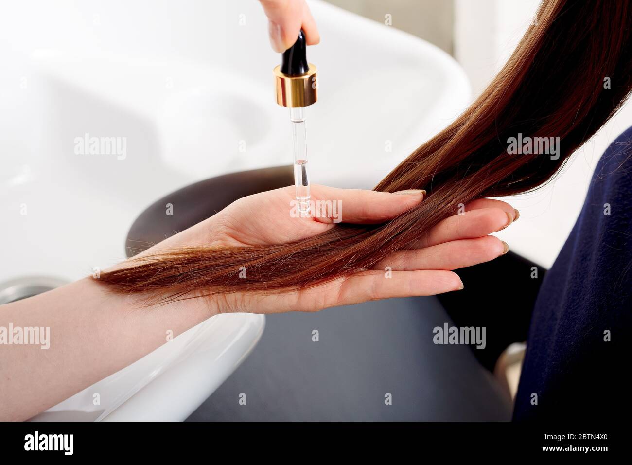 Mains de femmes appliquant de l'huile sur les longs poils bruns des femmes. Cosmétiques de soins capillaires, produits de beauté de bain. Sérum pour cheveux féminins pour le traitement des pointes de cheveux Banque D'Images