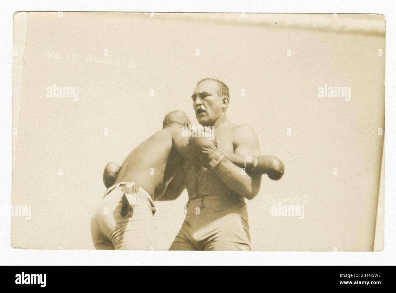 Carte postale photographique de Jack Johnson et James J Jeffries clinching. Carte postale photographique en noir et blanc du combat du siècle entre Jack Johnson et James J. Jeffries. Dans cette photo, la paire se tient debout de poitrine à poitrine avec des bras emboîtés. Banque D'Images